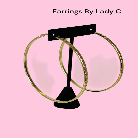 Gold hoop earrings on a black earring stand against a pink background with 'Earrings By Lady C' text.