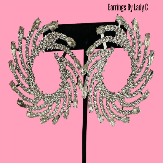 Pair of ornate earrings on a black stand against a pink background with 'Earrings By Lady C' text.