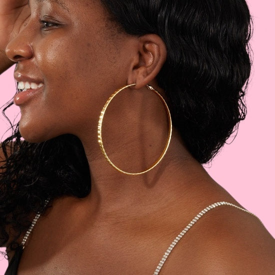 Woman wearing gold hoop earrings with a pink background