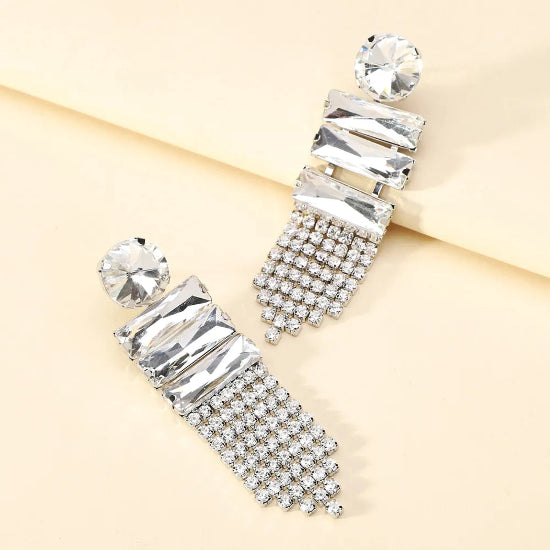 Pair of silver earrings with clear gemstones on a beige background