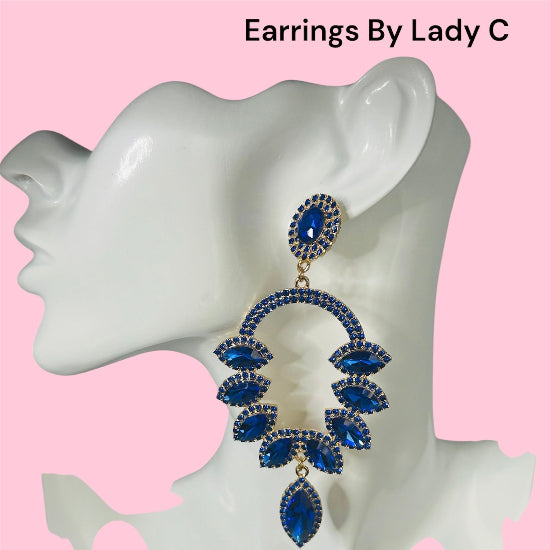 Blue earrings on a mannequin ear with 'Earrings By Lady C' text above, pink background