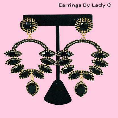 Black and gold earrings on a black stand with 'Earrings By Lady C' text on a pink background