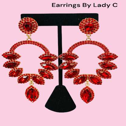 Red earrings on a black stand with 'Earrings By Lady C' text on a pink background