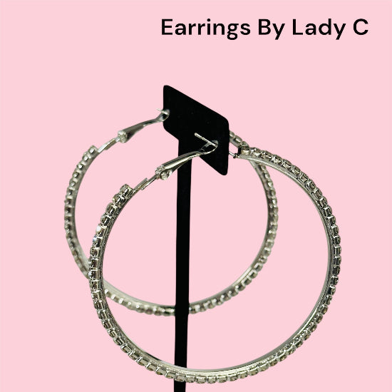 Pair of silver hoop earrings on a black stand against a pink background with 'Earrings By Lady C' text.