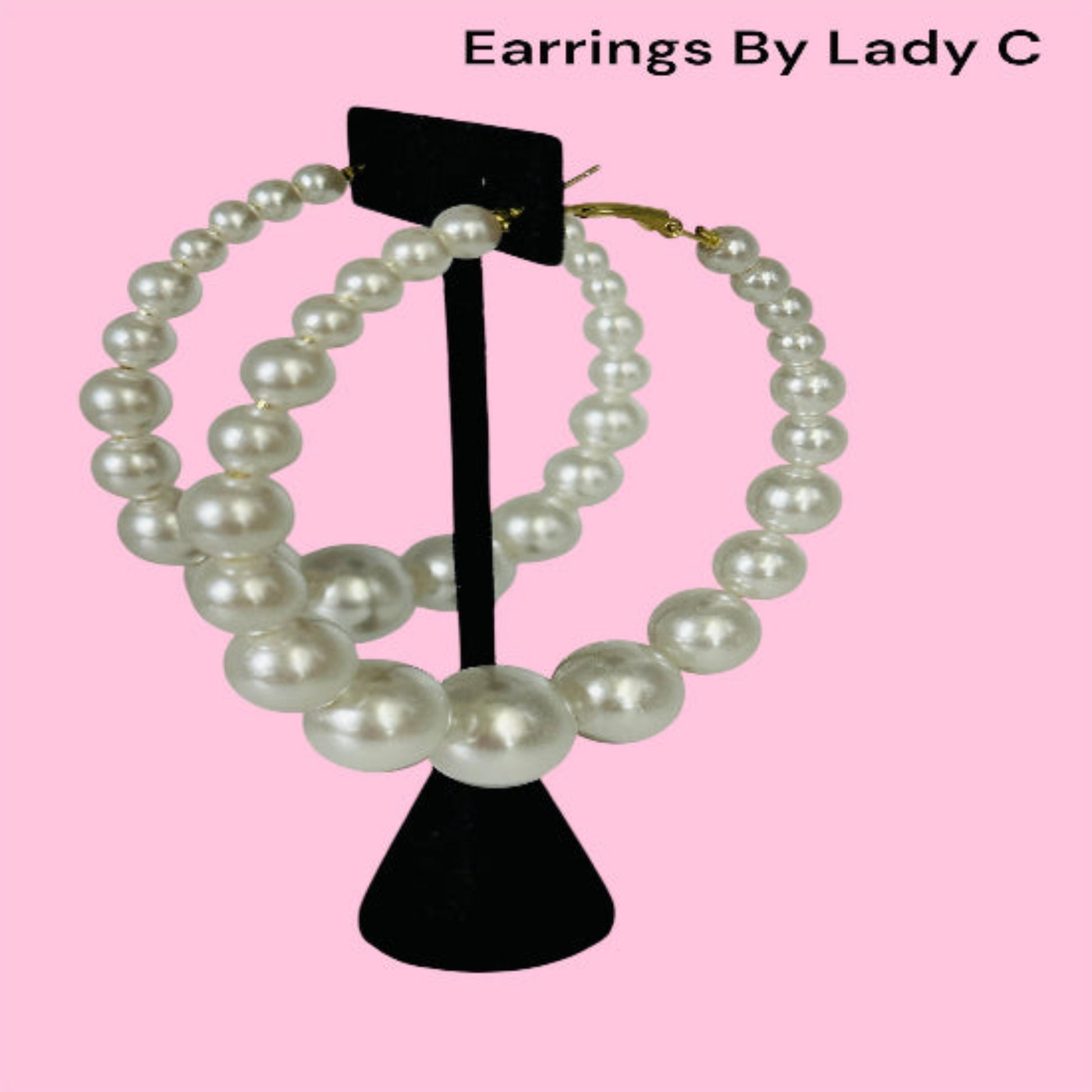 Pearl earrings on a black stand against a pink background.