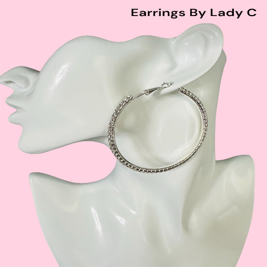 Silver hoop earrings on a mannequin ear with a pink background, branded 'Earrings By Lady C'.