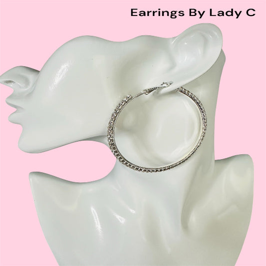 Silver hoop earrings on a mannequin ear with a pink background, branded 'Earrings By Lady C'.