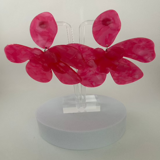 Large flower-shaped stud earrings in vibrant hot pink, featuring bold, detailed petals with a glossy finish. 