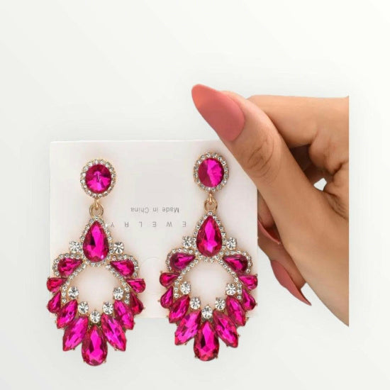 Pink gemstone earrings held by a hand on a white background